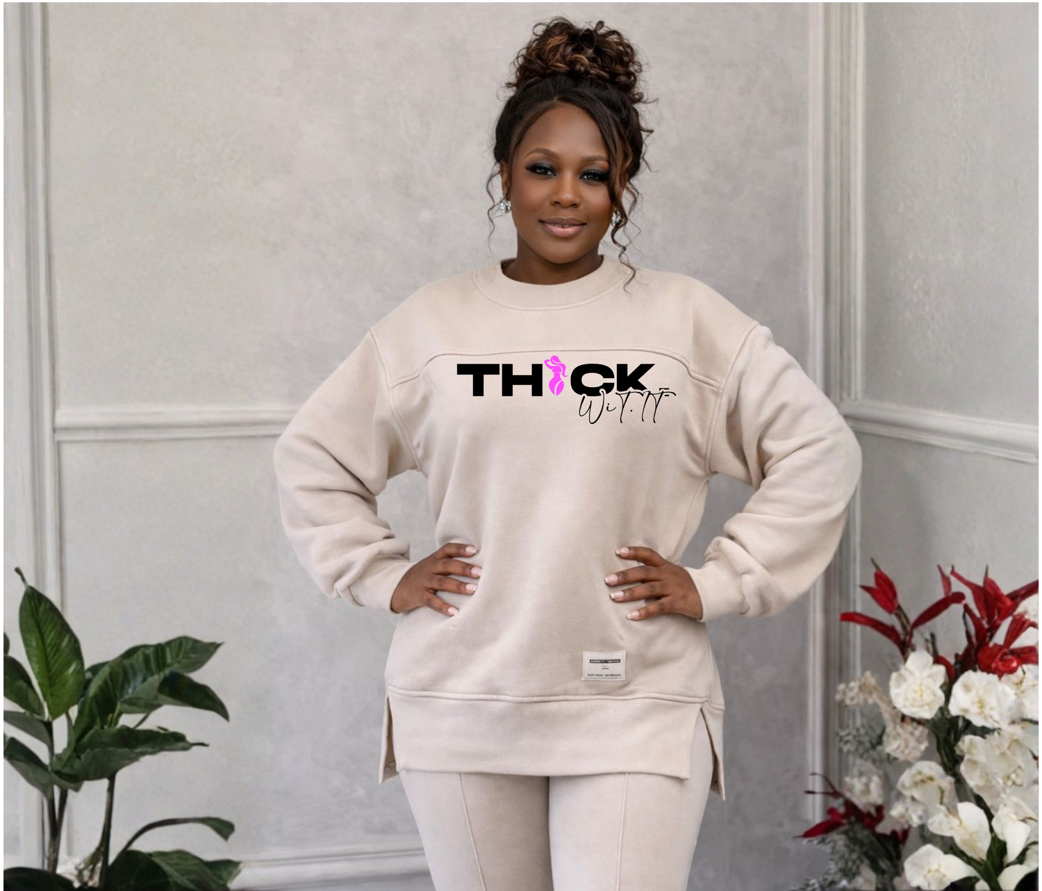 Earline Strickland standing confidently with hands on hips, wearing a cream oversized sweatshirt and matching pants with the ‘Thick Wit It’ logo on the chest, styled in a neutral indoor setting