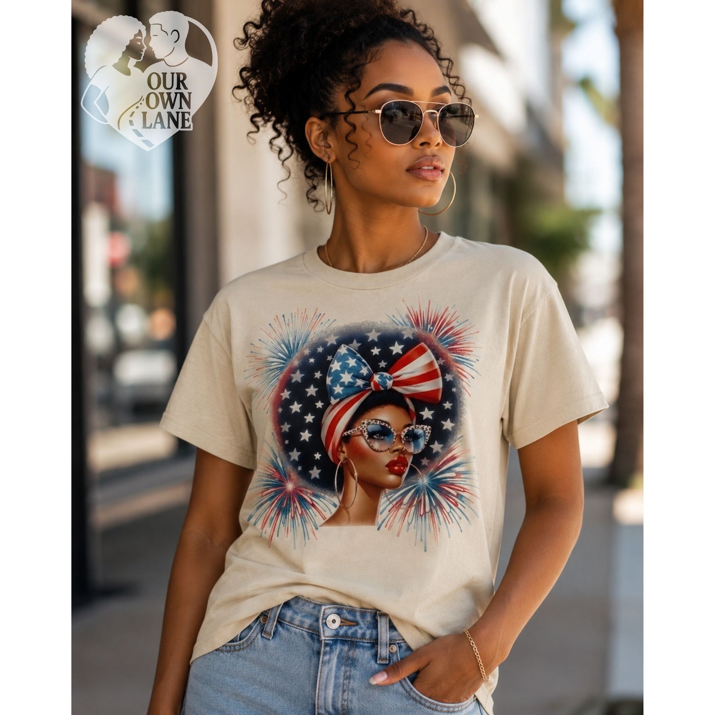 Sand color unisex t-shirt featuring patriotic glam graphic with stylish woman wearing star bow headwrap, cat-eye glasses, and fireworks background by Our Own Lane