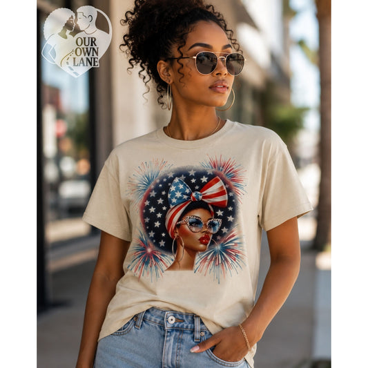 Sand color unisex t-shirt featuring patriotic glam graphic with stylish woman wearing star bow headwrap, cat-eye glasses, and fireworks background by Our Own Lane
